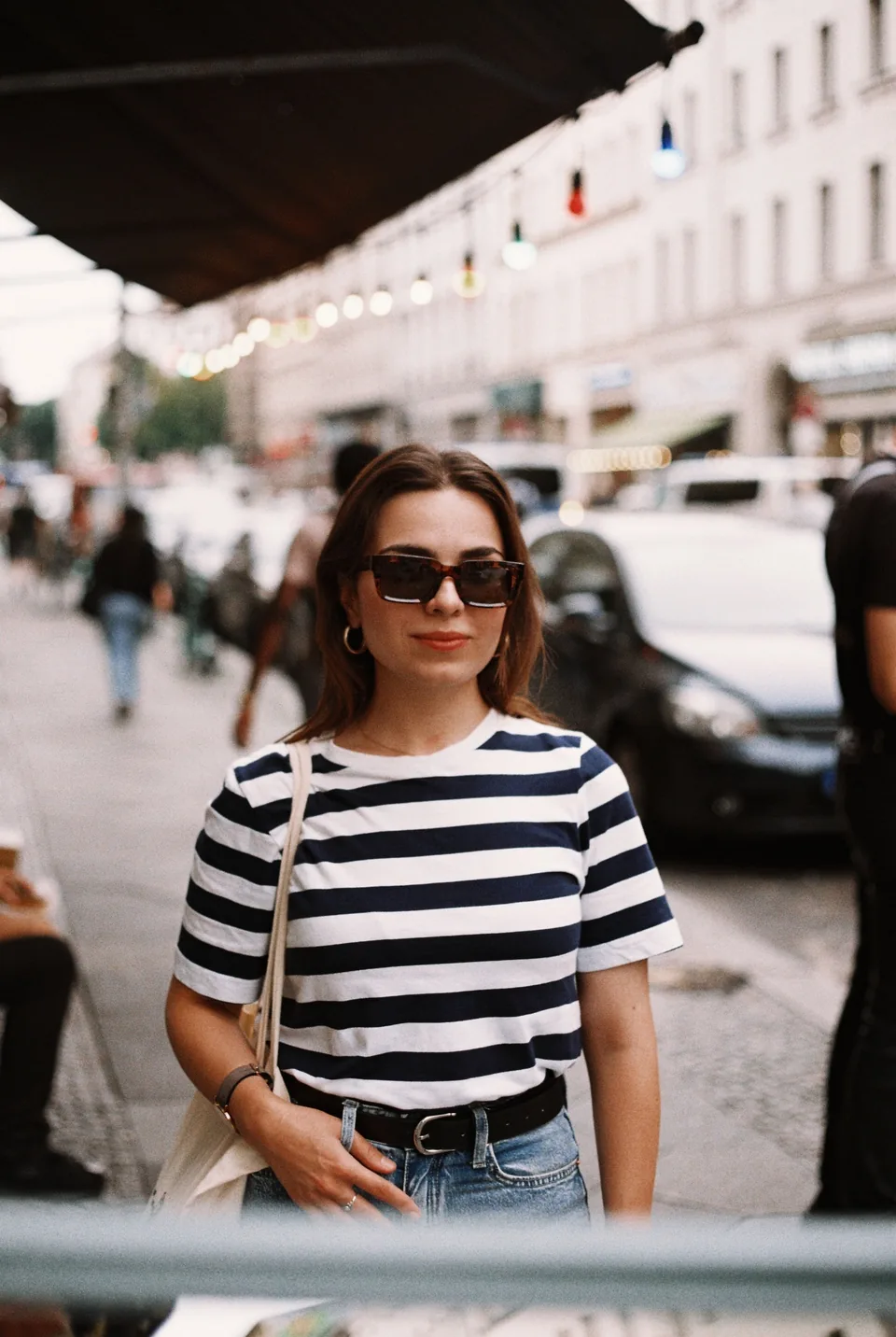 Woman in sunglasses, a striped tee and a tote bag on a busy street