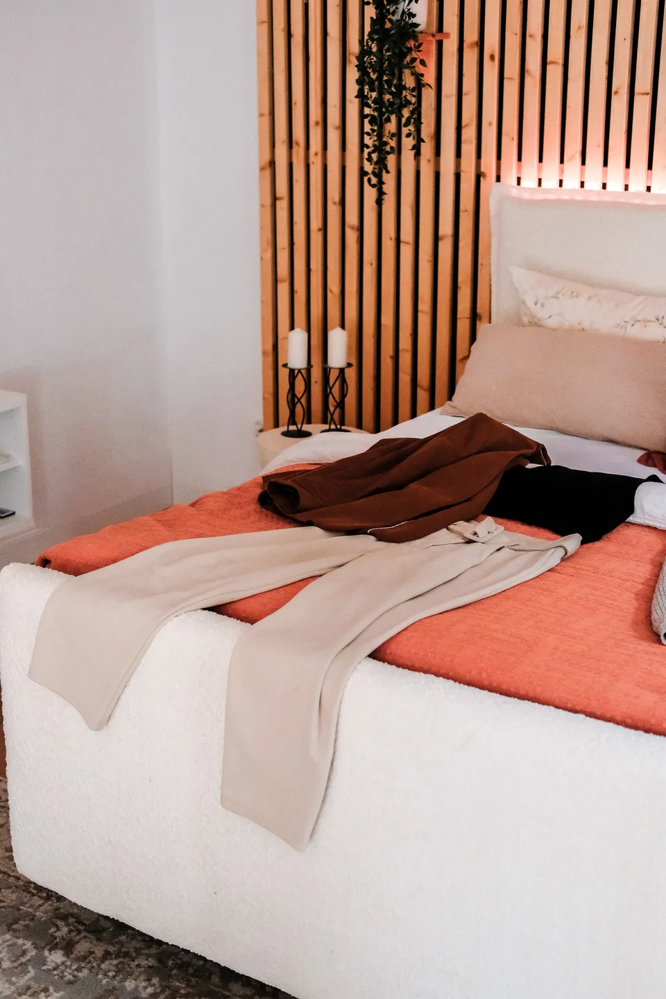 Outfit laid out on a bed: beige trousers, a brown jacket and a black top on a coral blanket